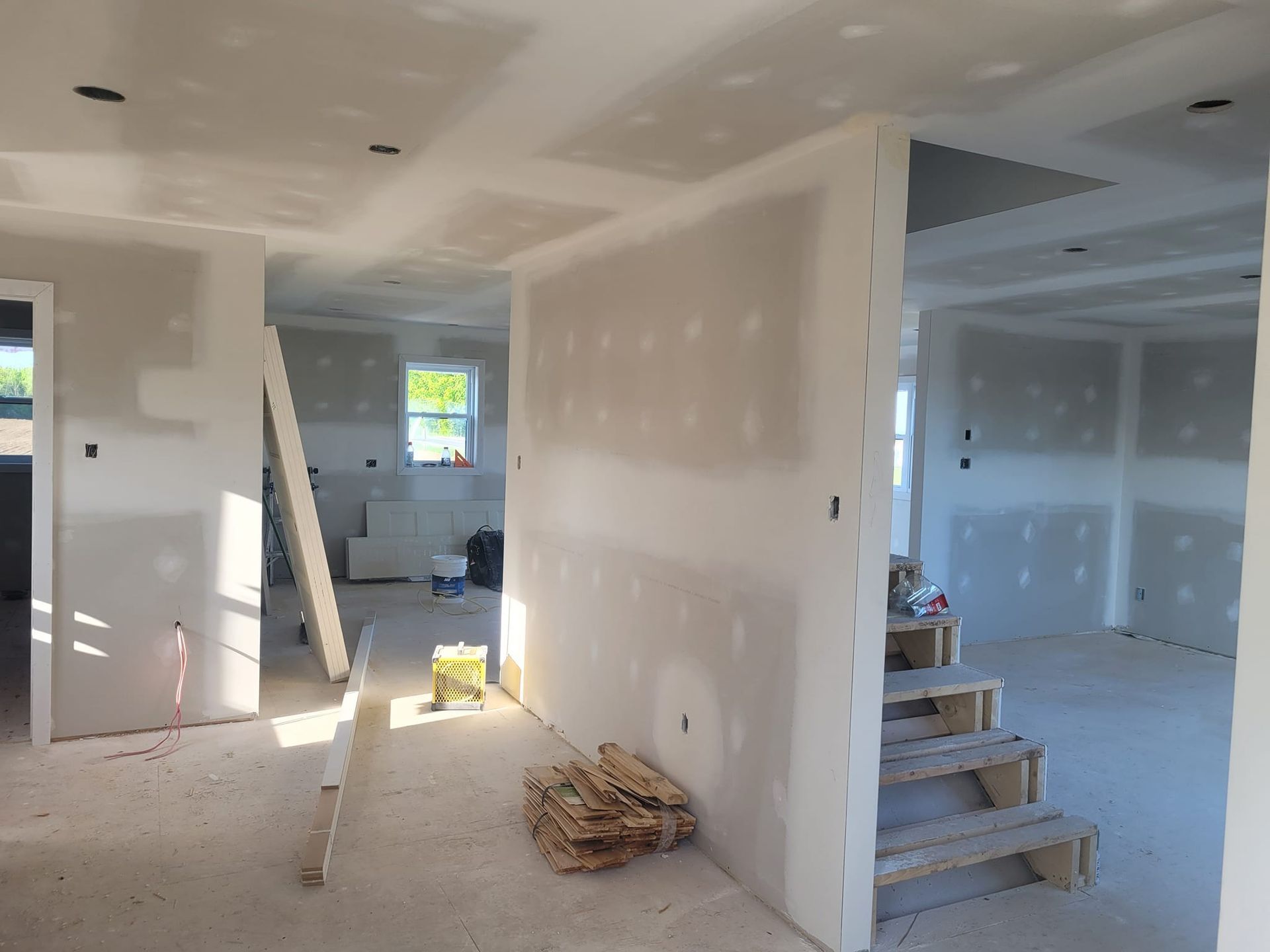 Une pièce en cours de rénovation avec des cloisons sèches et des escaliers.