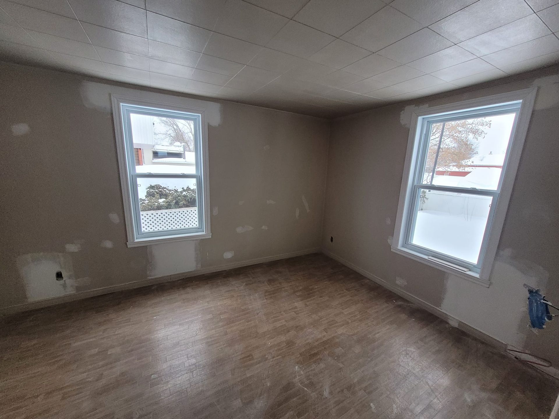 Une pièce vide avec deux fenêtres et un plancher en bois.