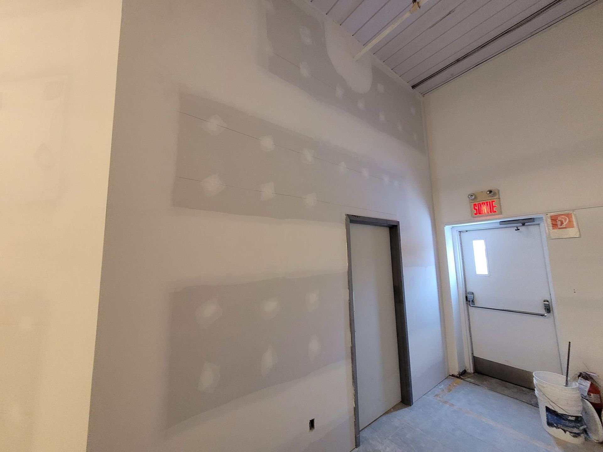 Une pièce avec une porte et un panneau de sortie rouge sur le mur.