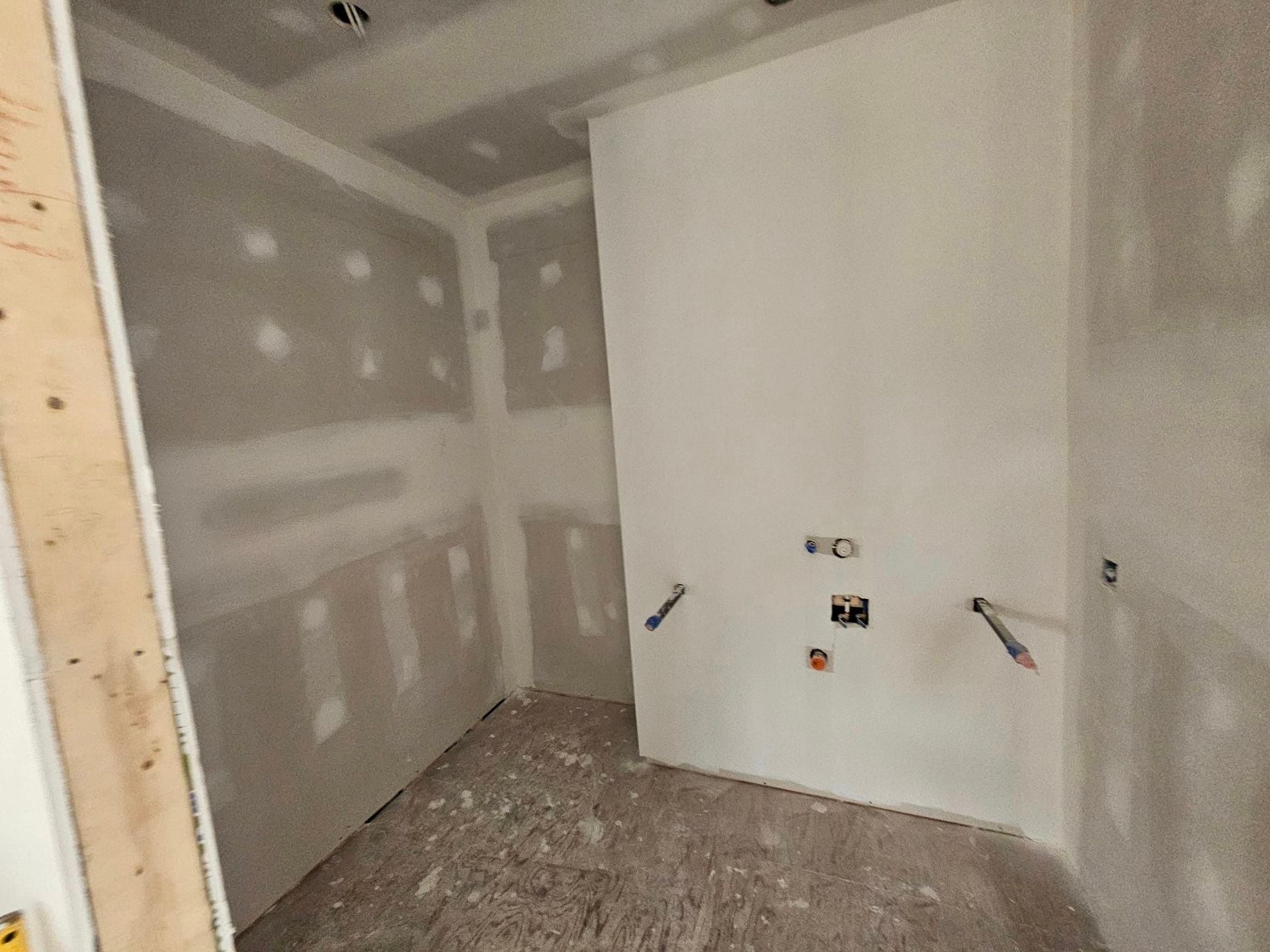 Une pièce avec des cloisons sèches sur les murs et une porte en bois.