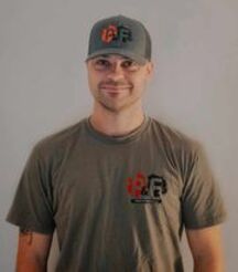 Un homme portant un chapeau et un t-shirt se tient devant un mur blanc.