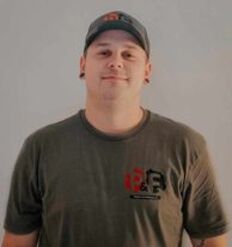 Un homme portant un chapeau et un t-shirt se tient devant un mur blanc.