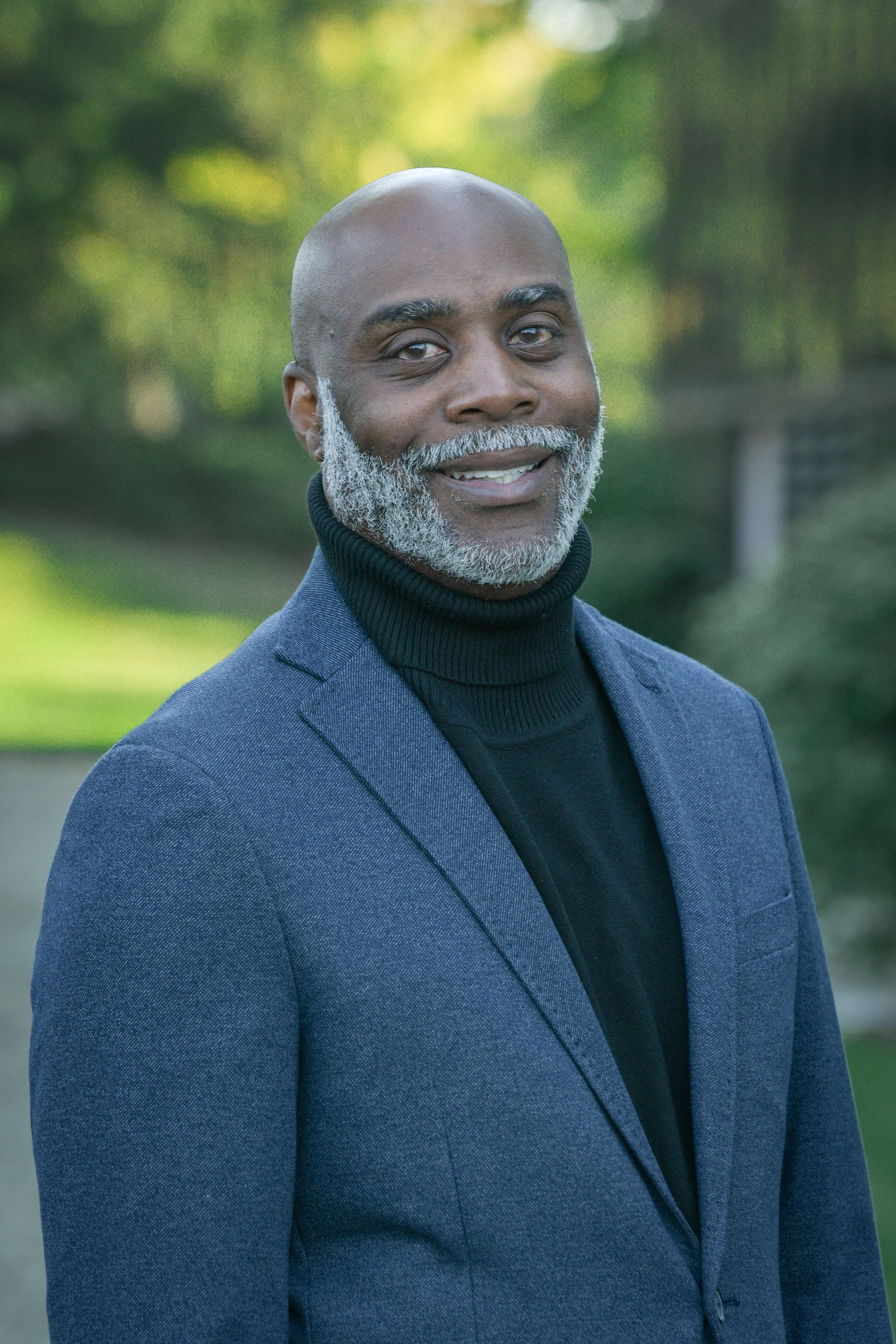 A man in a suit and turtleneck is smiling for the camera.