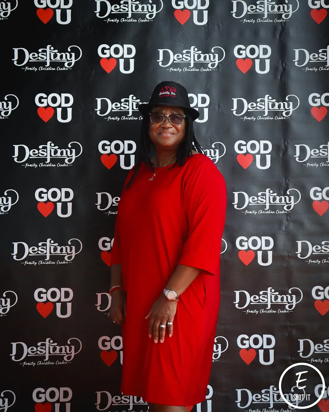 A woman in a red dress stands in front of a wall that says god destiny