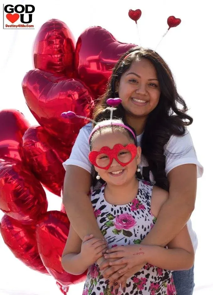 A woman is hugging a little girl who is wearing heart shaped glasses