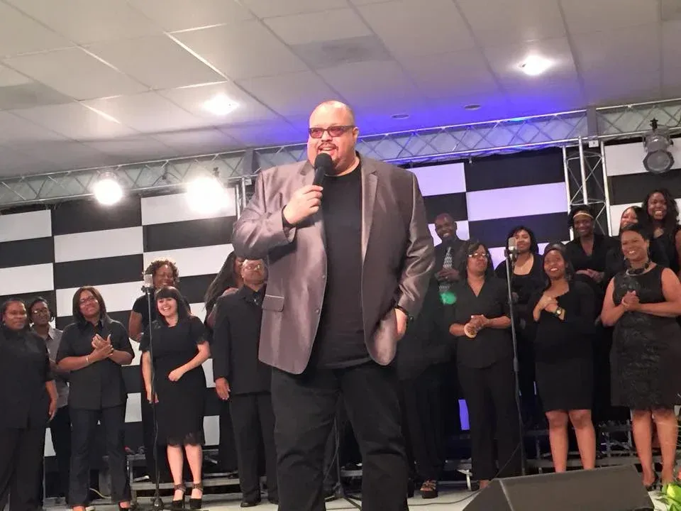 A man is standing in front of a choir holding a microphone.