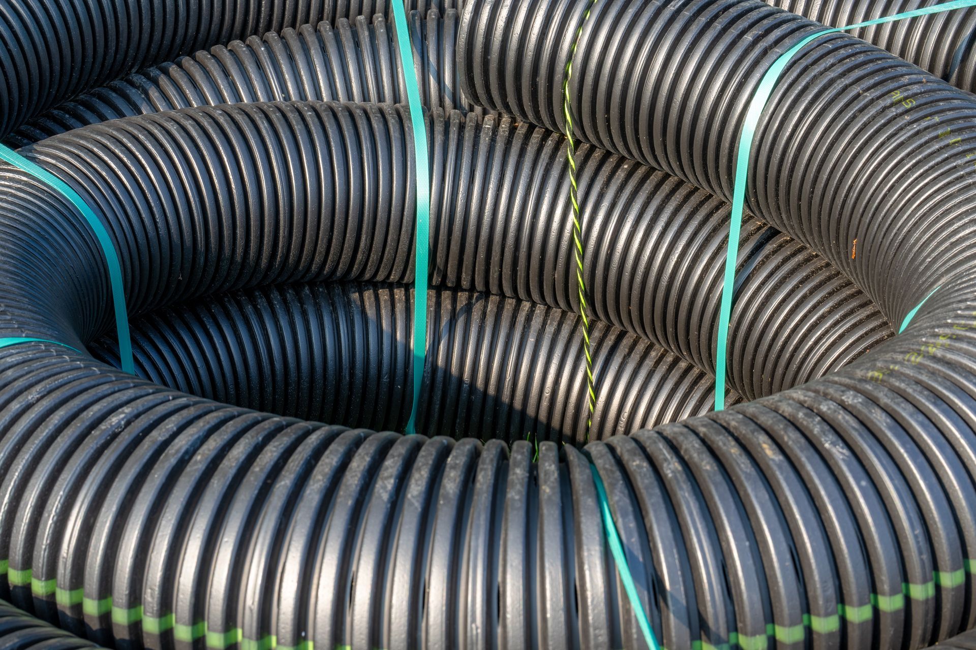Coiled black corrugated drainage pipes secured with green straps.