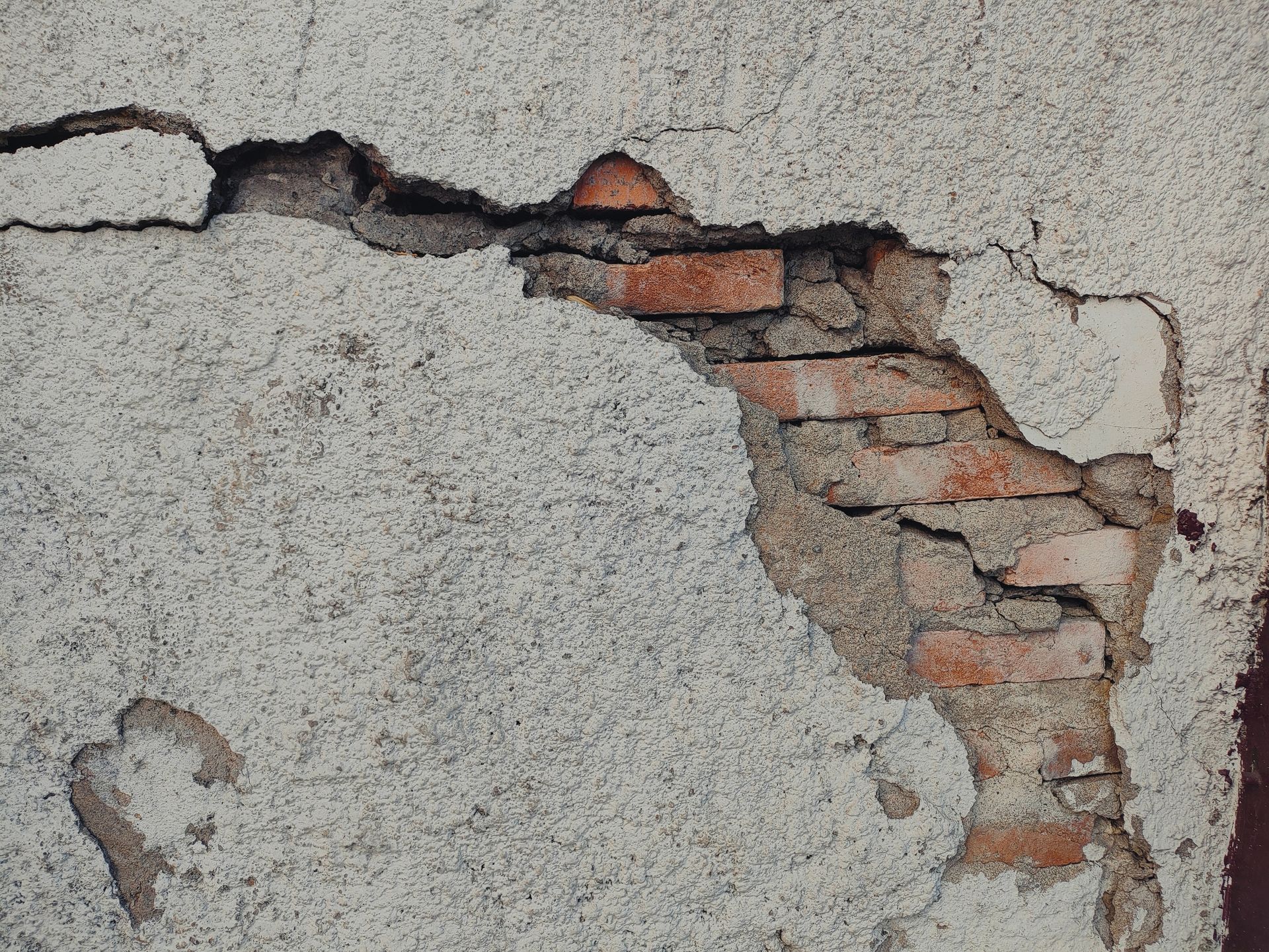 Damaged exterior wall, showing crumbling stucco revealing brick underneath.