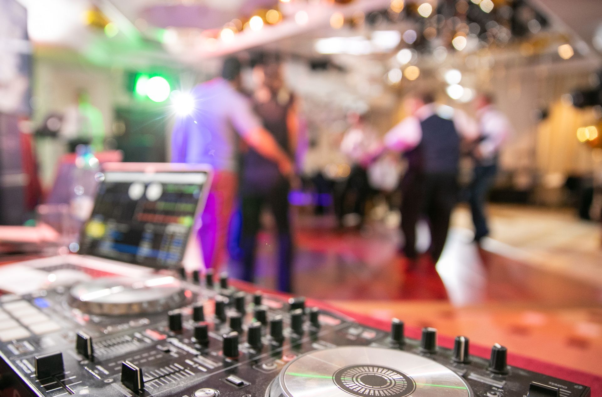 A DJ is playing music at a wedding with people dancing in the background.