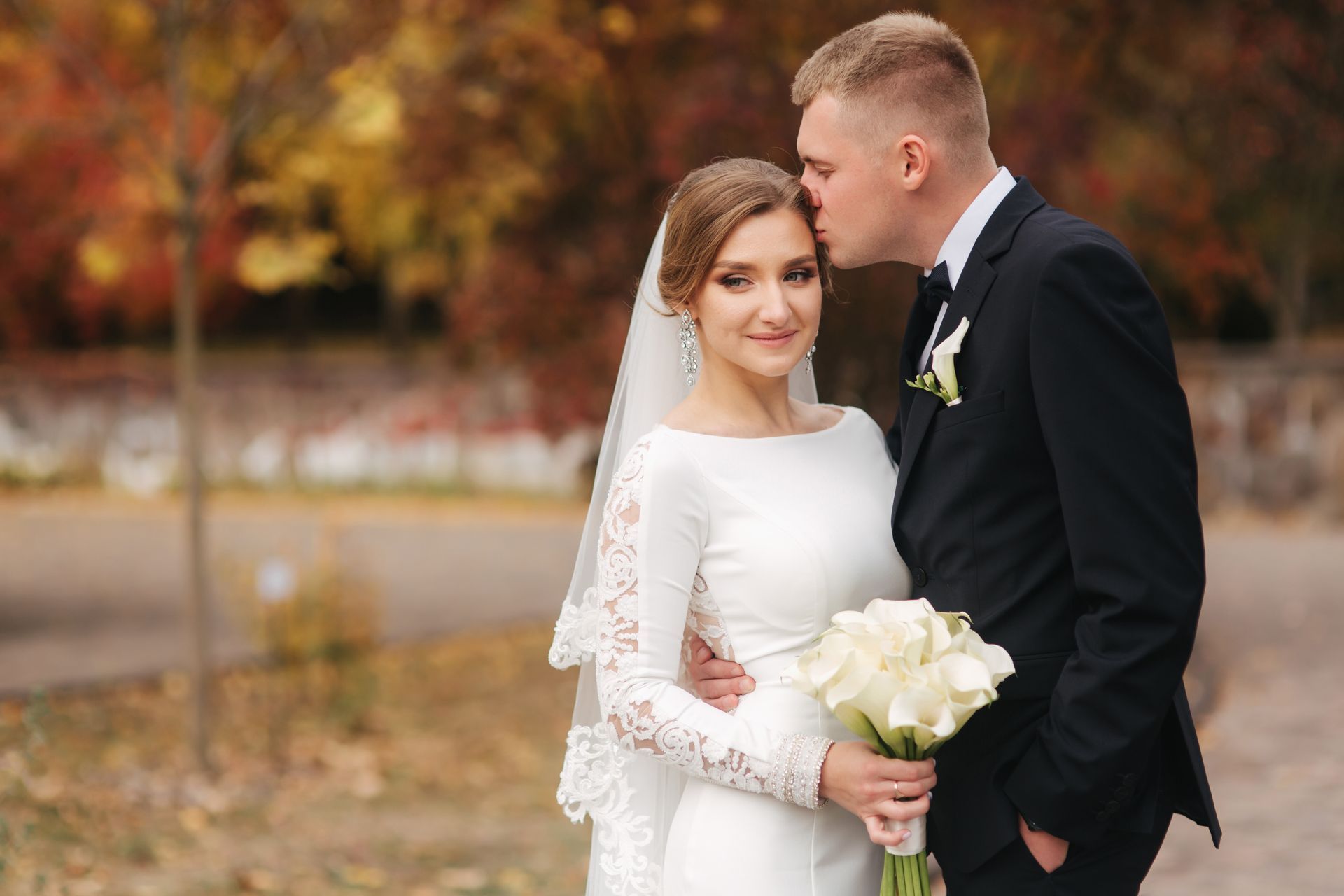 Groom kisses bride's forehead outside surrounded by fall foliage in Crittenden, KY