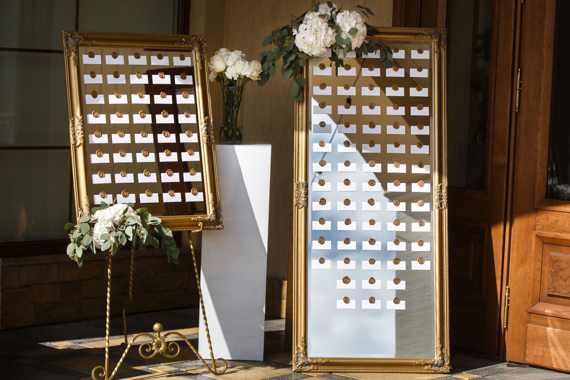 Two golden mirrors with floral accents displaying escort cards at a wedding