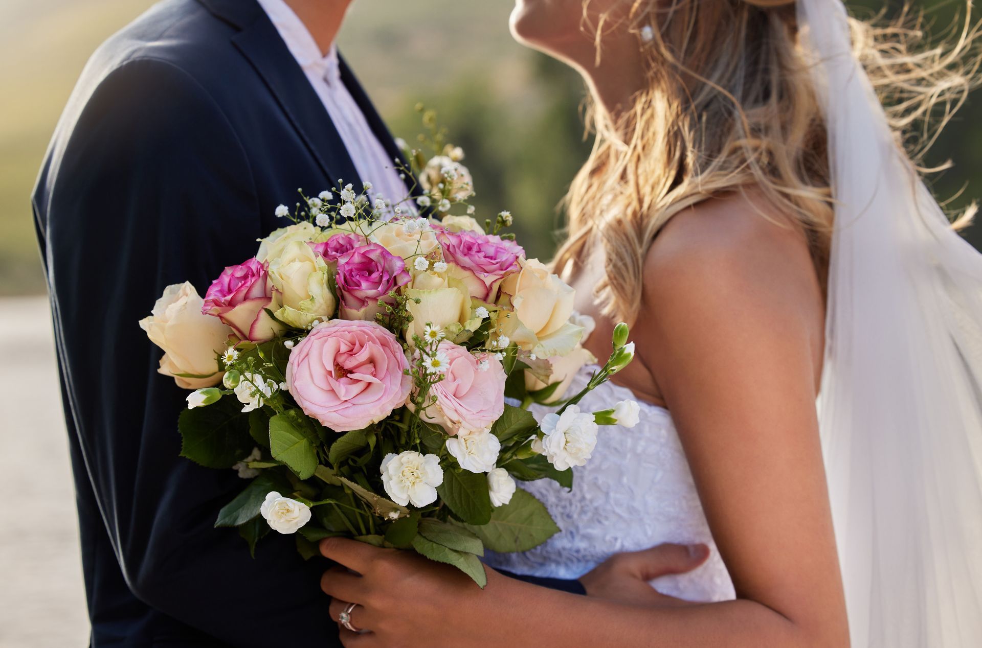 Close up of a bride and groom embracing on their wedding day with a bouquet of pink and white flowers