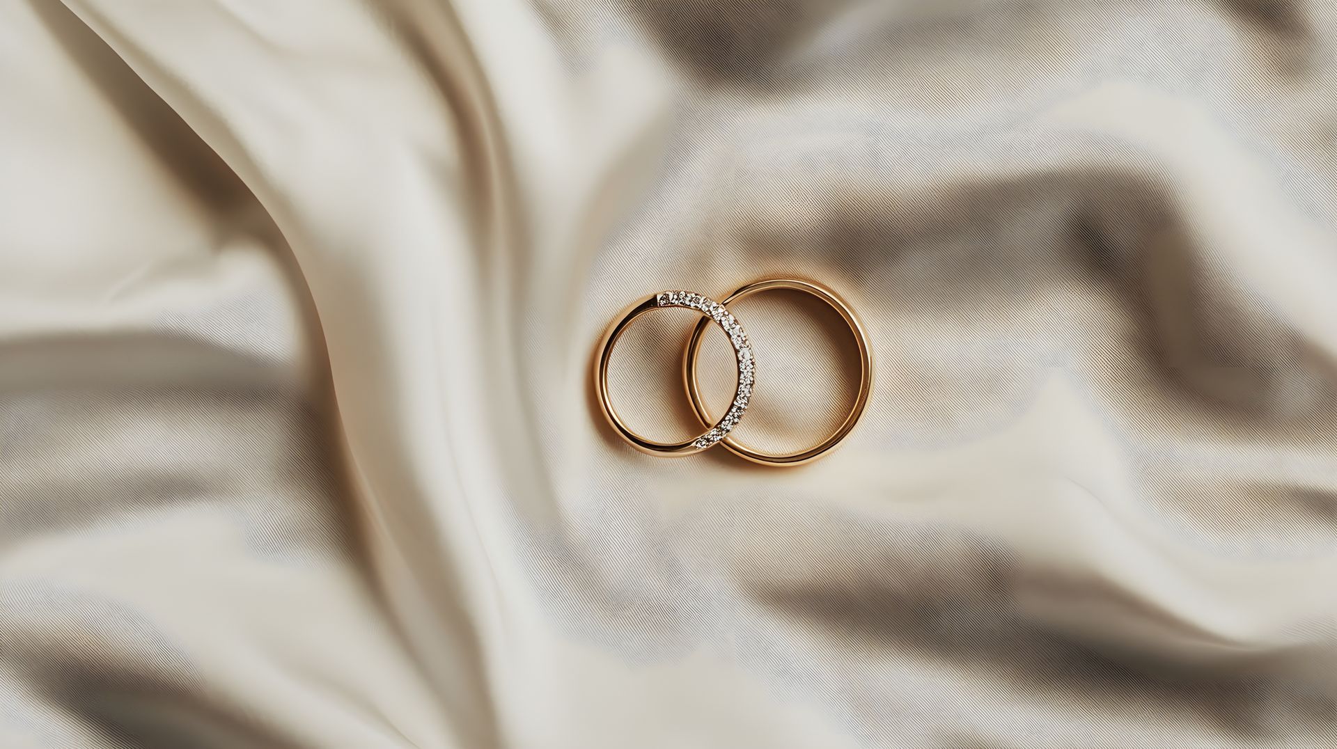 Detail shot of two gold wedding bands on an ivory satin fabric background