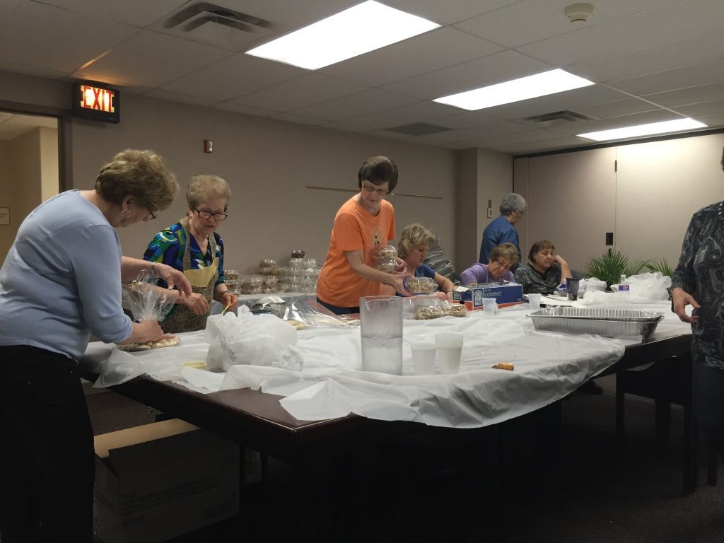 A group of women in a room gather around tables and packing food items.
