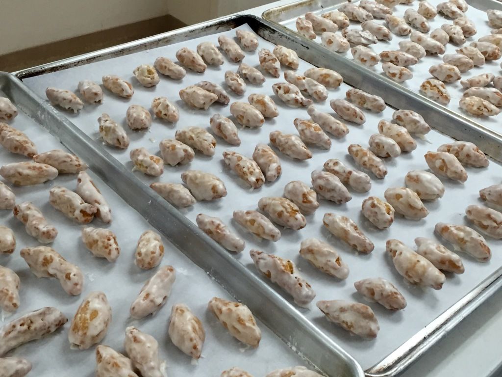 Rows of glazed pastries are organized neatly on three baking trays.