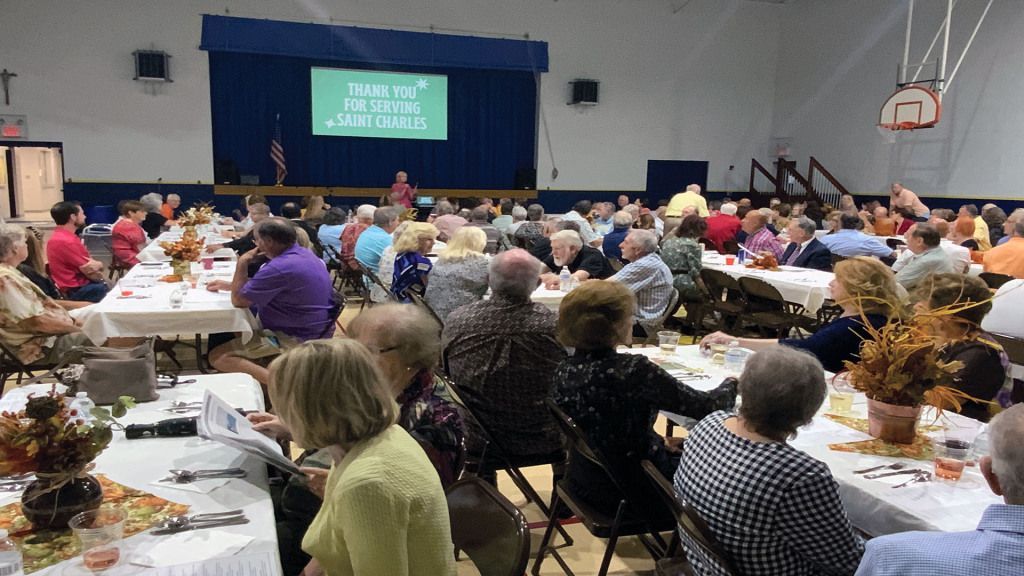 A large gathering in a hall features people seated at long tables. A large gathering in a hall features people seated at long tables.