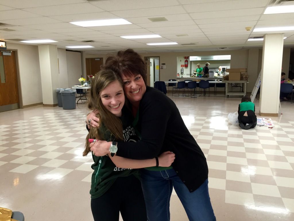 A woman and a girl smiling and hugging in a large room with a checkered floor.