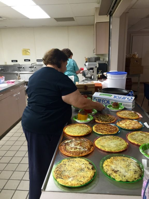 A woman prepares multiple quiches on a stainless steel counter in a commercial kitchen. 