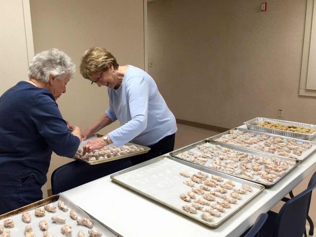 Two elderly women in casual clothing happily bake together, arranging cookies on trays.