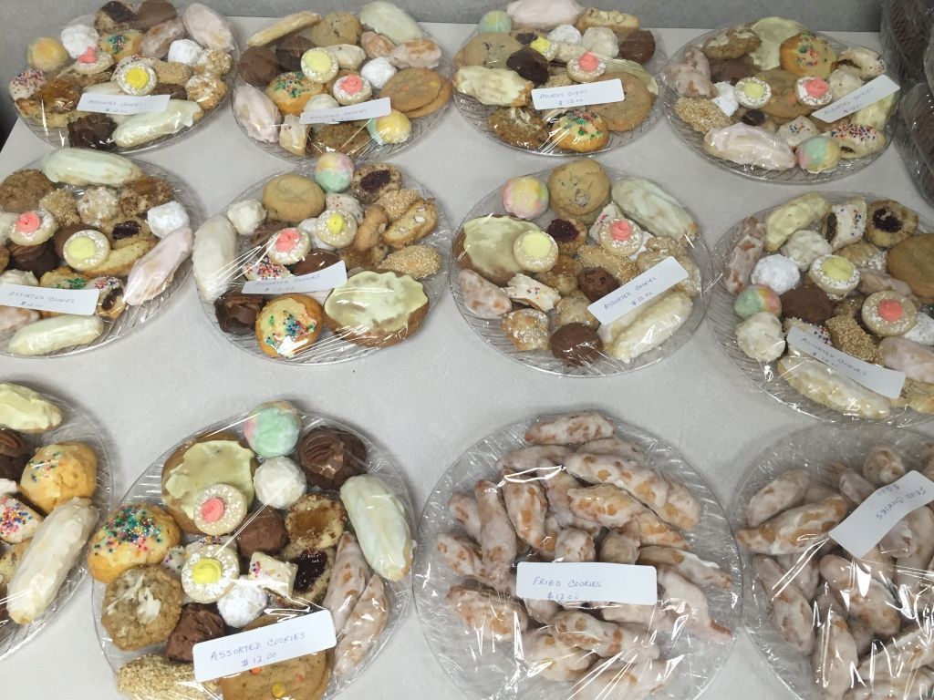 Plates of assorted cookies wrapped in plastic on a table. 