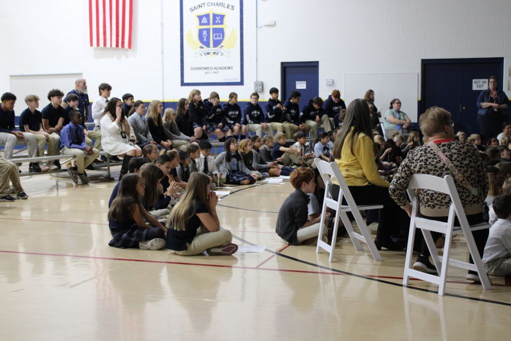 A group of students sits on a gym floor.