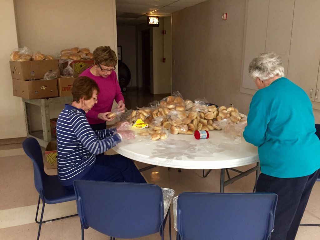Three elderly women are sorting bread rolls on a round table.