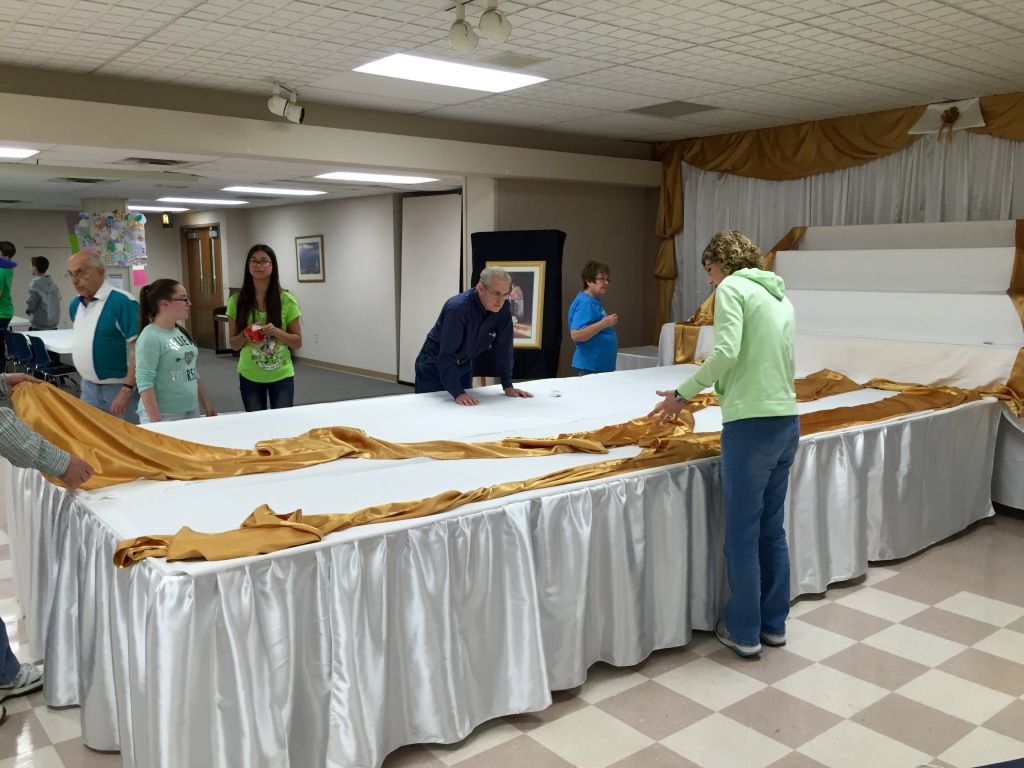 Group of people arranging gold and white table drapes in a hall. 