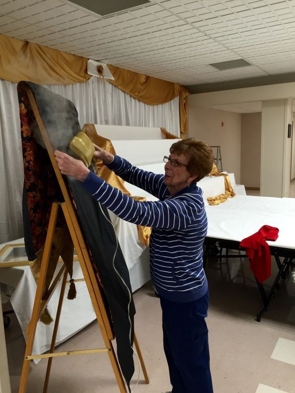 A woman in a striped sweater uses a steamer on a fabric piece draped over a wooden frame. 