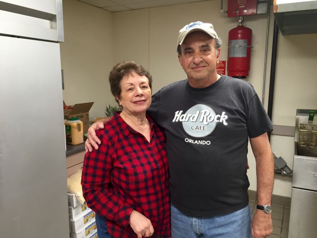 A smiling couple stands in a kitchen. 