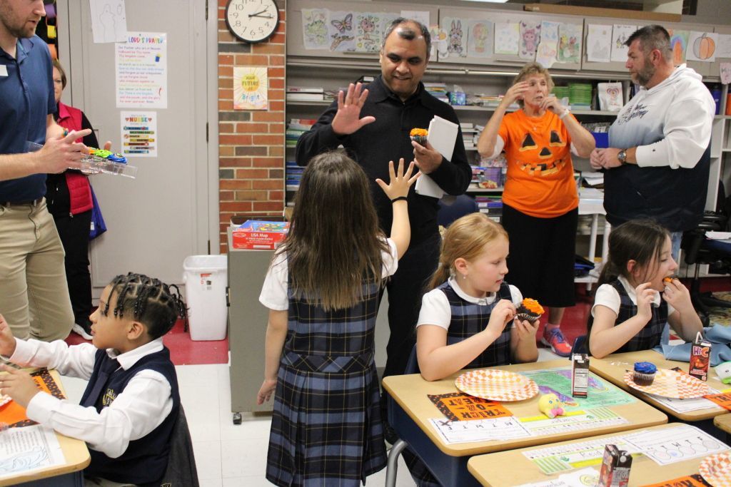 Children in uniforms eat cupcakes at their desks.