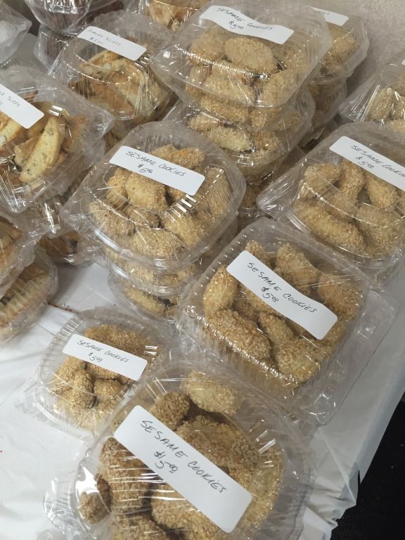 Clear plastic containers filled with sesame cookies are stacked on a table. 