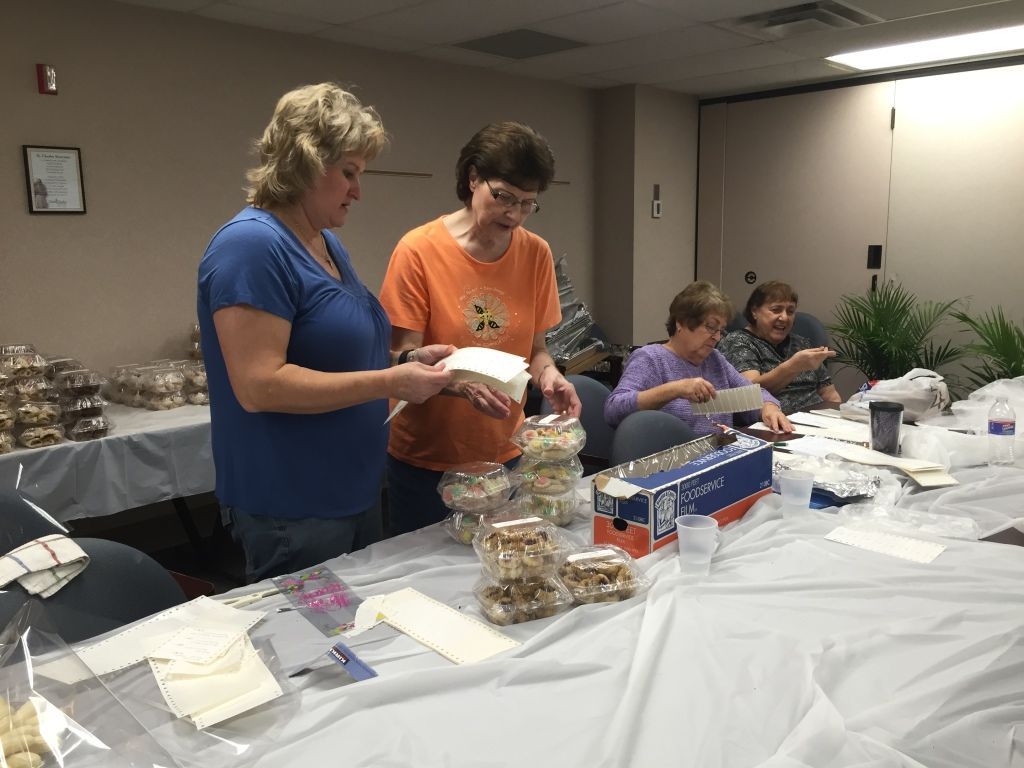Four women gather around a table covered with baked goods and packaging materials.
