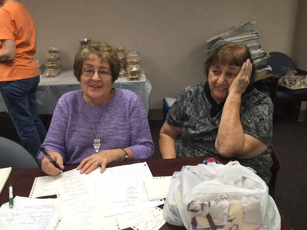 Two women sit at a table covered with papers and notes.