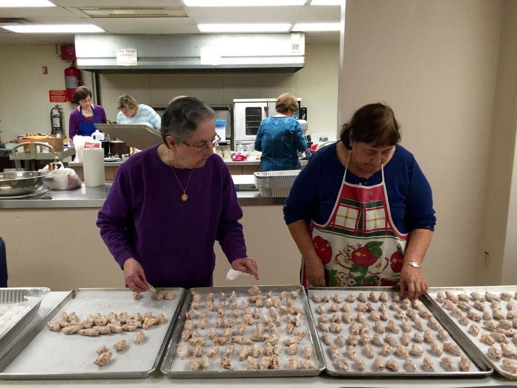 Women in a kitchen preparing multiple trays of baked goods.