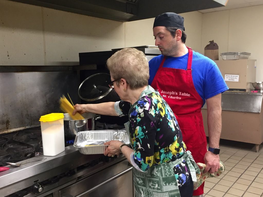 A woman and a man, both wearing aprons, are cooking in a kitchen.