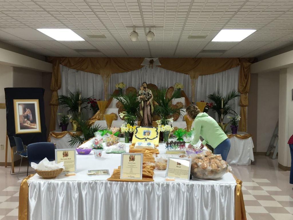 A decorative altar in a hall features a statue surrounded by plants, flowers, and bread offerings.