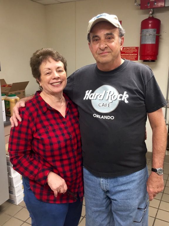 A smiling couple stands in a kitchen. 