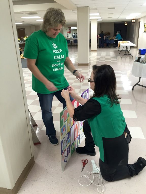 Two women prepare a colorful poster in a hallway. 