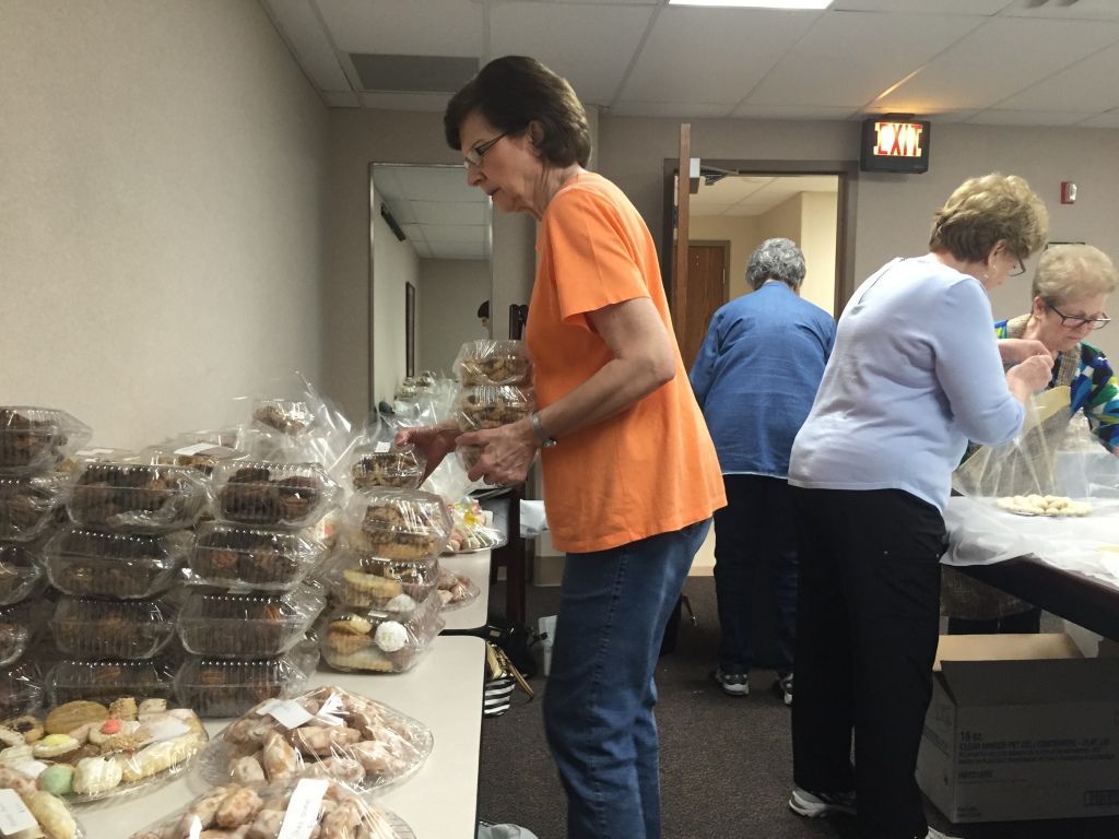 A woman in an orange shirt sorts baked goods in plastic containers on a table.