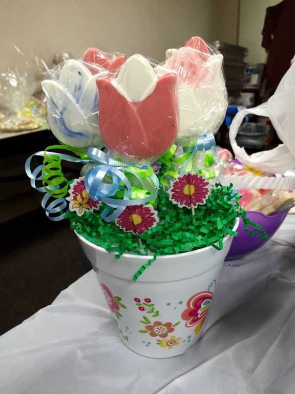A white pot with colorful flower designs holds tulip-shaped lollipops.
