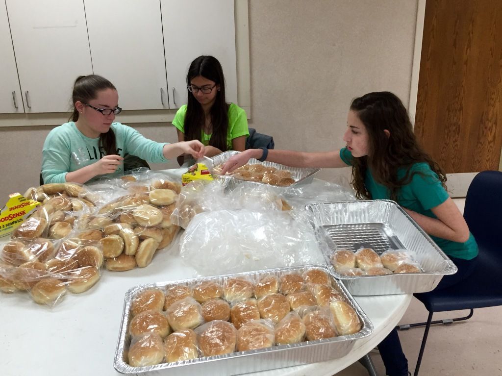 Three young people are seated around a table sorting bread rolls into trays. 