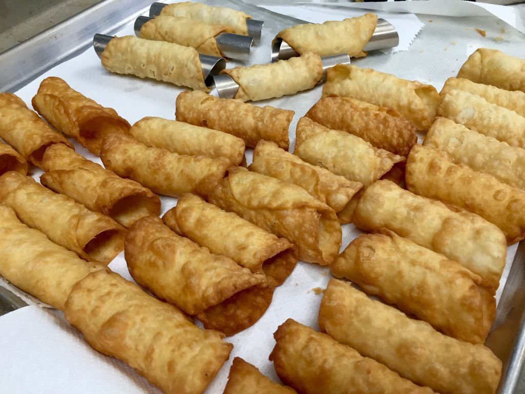 A tray of freshly fried cannoli shells, golden and crispy, lies on paper towels to drain oil. 