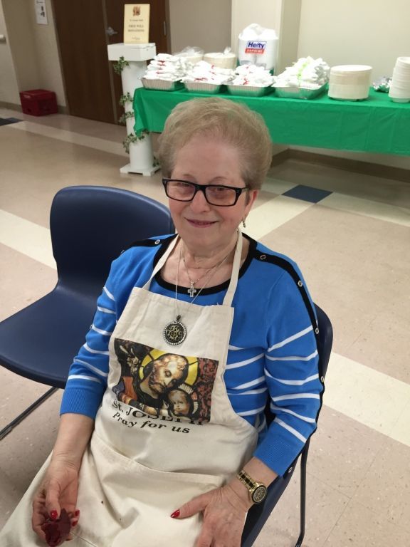 An elderly woman with glasses smiles while seated indoors. 