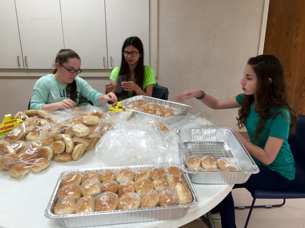 Three young people are seated around a table sorting bread rolls into trays. 