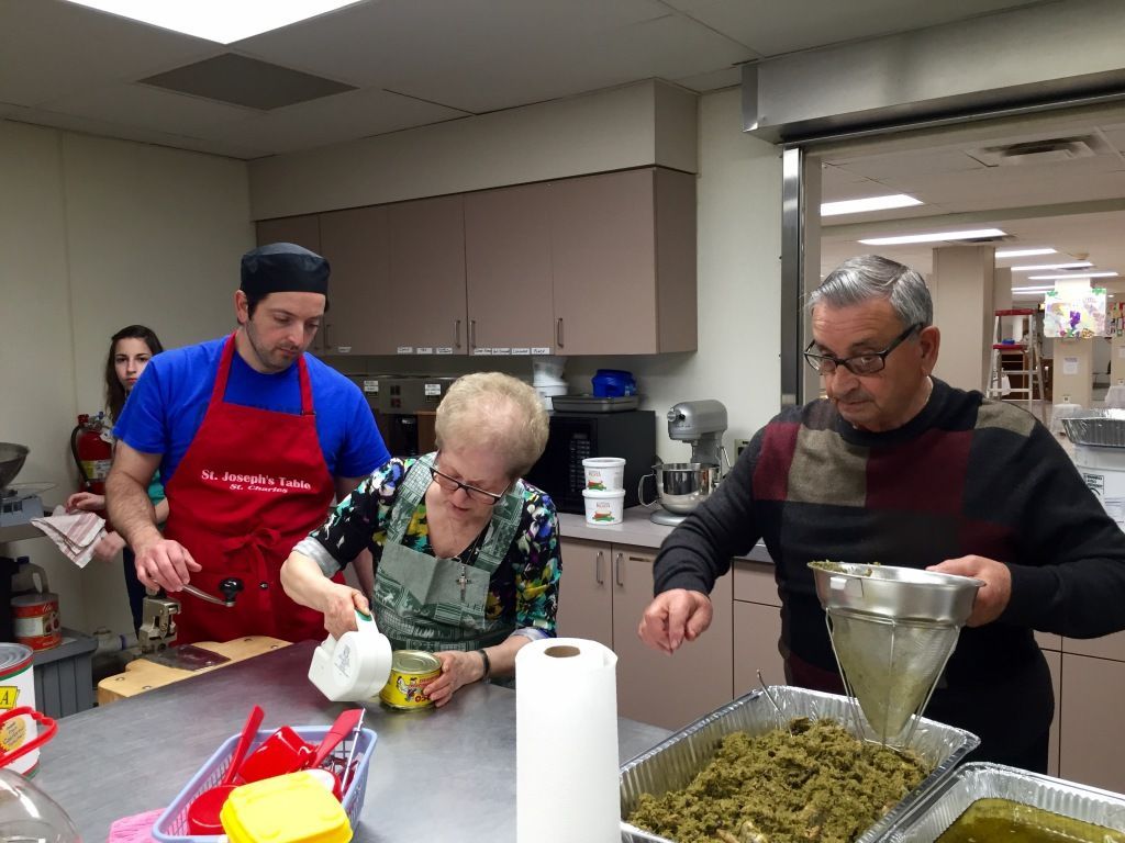Three adults cook in a kitchen.