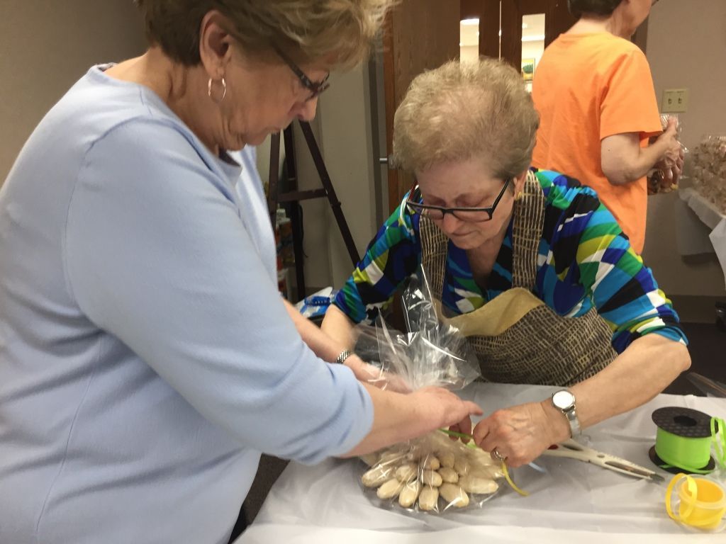 Two older women are packaging cookies in clear bags on a table. 
