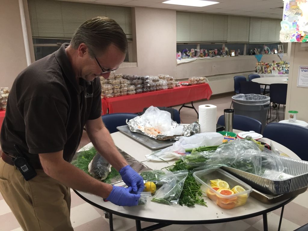 A man wearing a brown shirt and blue gloves prepares food at a table.