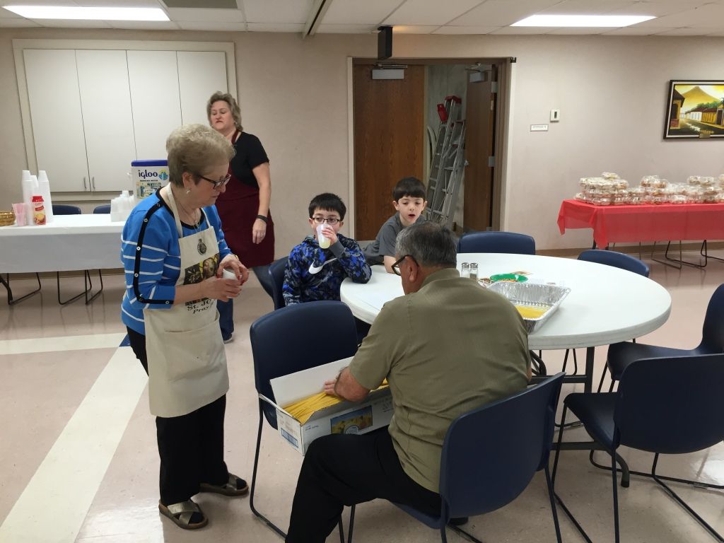 A community event setup with a woman in an apron talking to a seated man sorting food items.