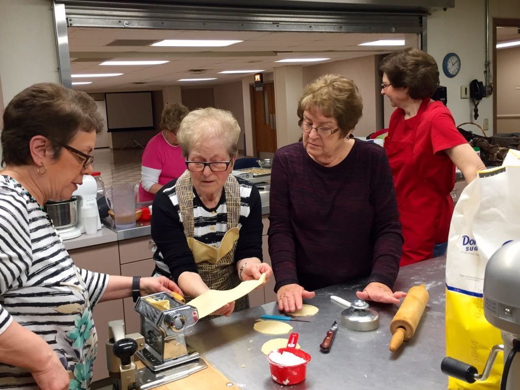 A group of older women in a kitchen, engaged in making dough.