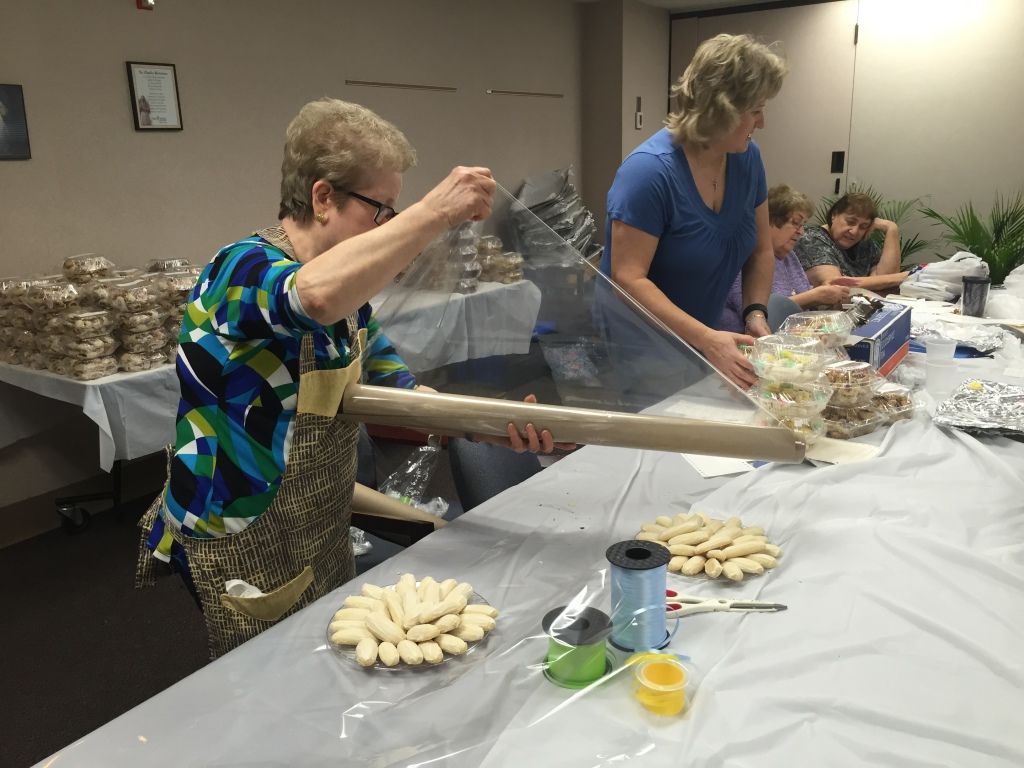 Women in a kitchen setting wrap cookies in clear plastic. 